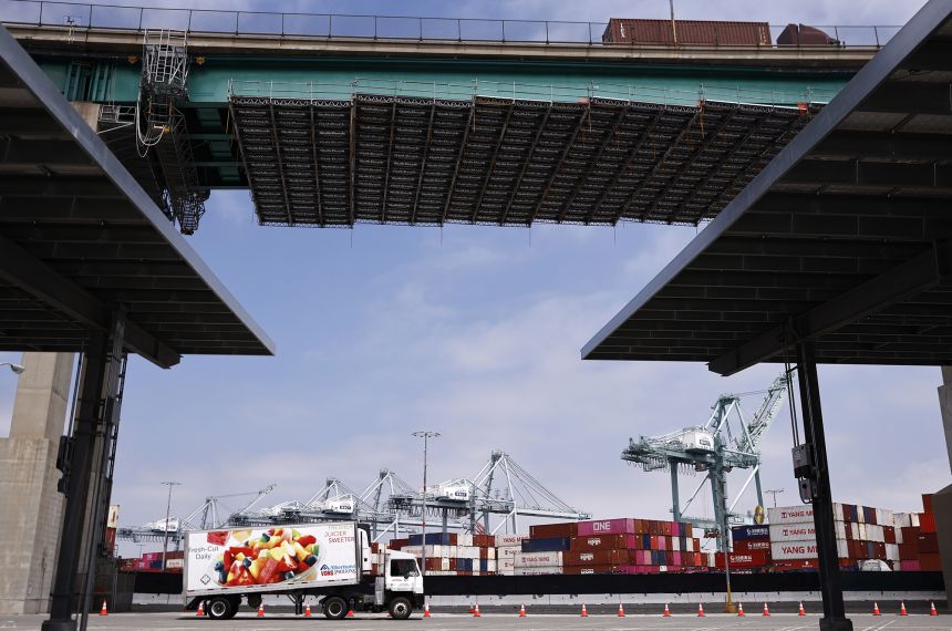 Trucks pass shipping containers stacked at the Port of Los Angeles on May 8, 2026.