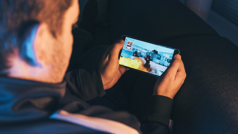 man blurred out, playing action video game on smartphone