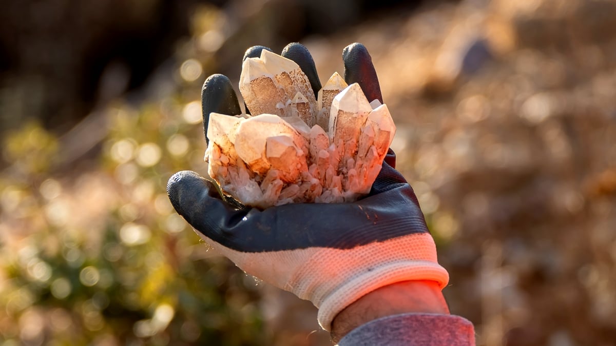 A gloved hand holds a cluster of pale quartz crystals outdoors in warm light.