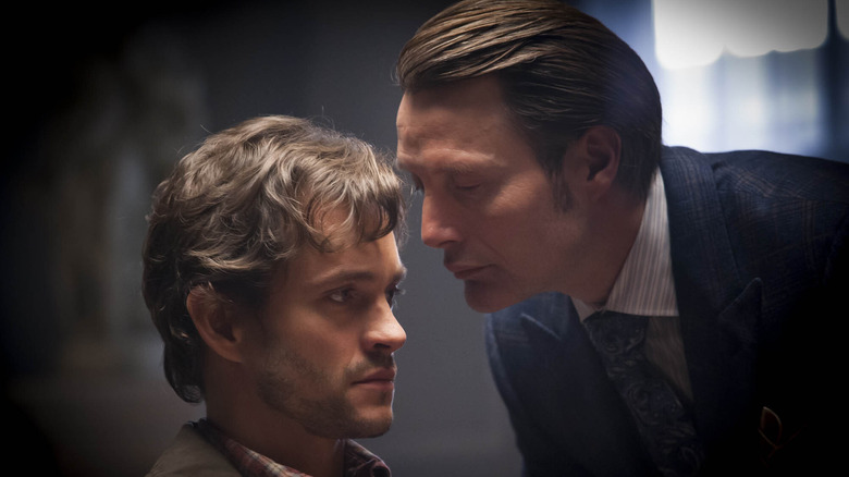 Will Graham (Hugh Dancy) sits and stares impassively ahead as Hannibal Lecter (Mads Mikkelsen) whispers in his ear in Hannibal