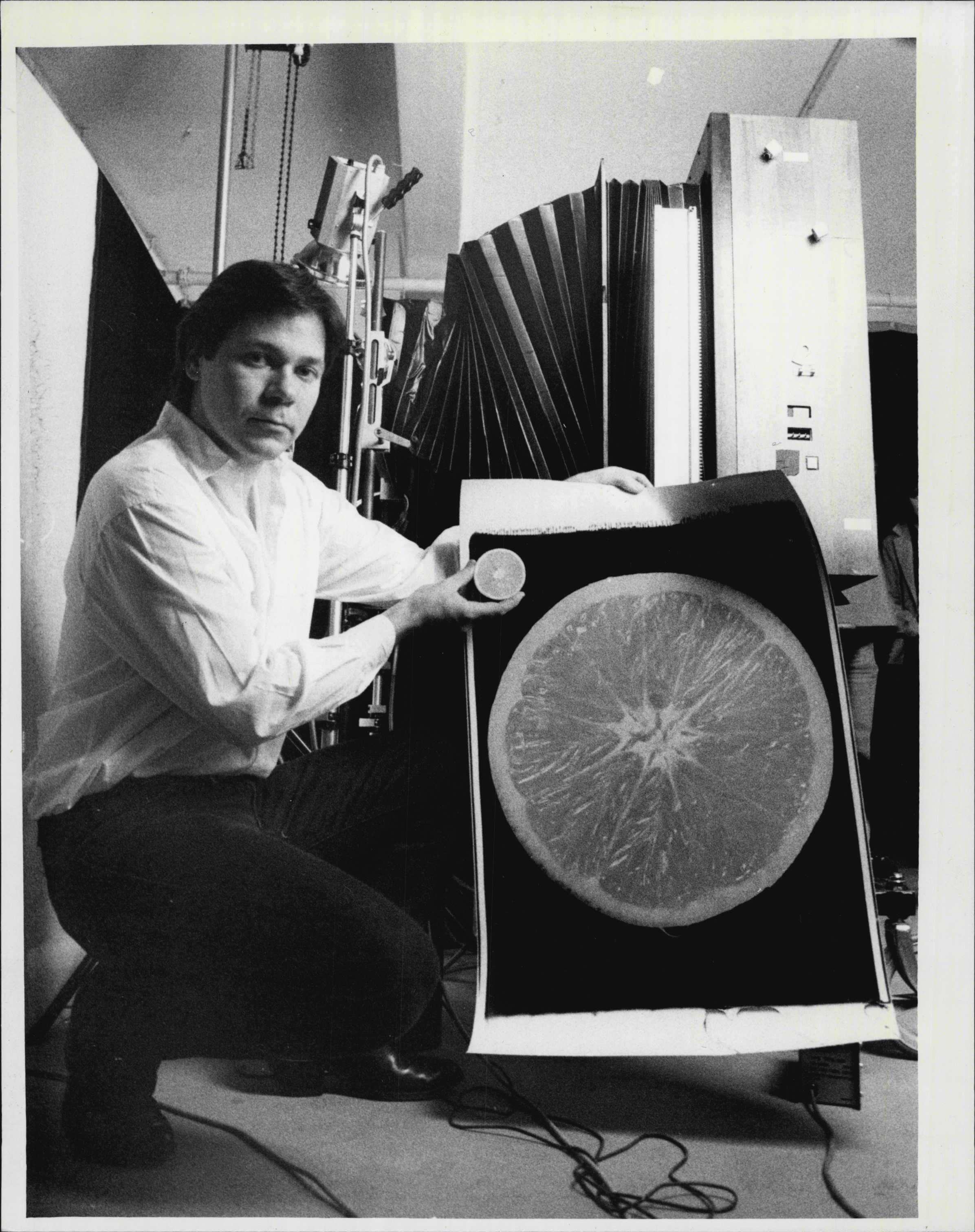 John Reuter, a Photographic Artist from the U.S. Demonstrates a 20x24 Polaroid Camera. He is pictured here with a shot of half orange taken with the camera. May 21, 1985. (Photo by Victor Colin Sumner/Fairfax Media via Getty Images).
