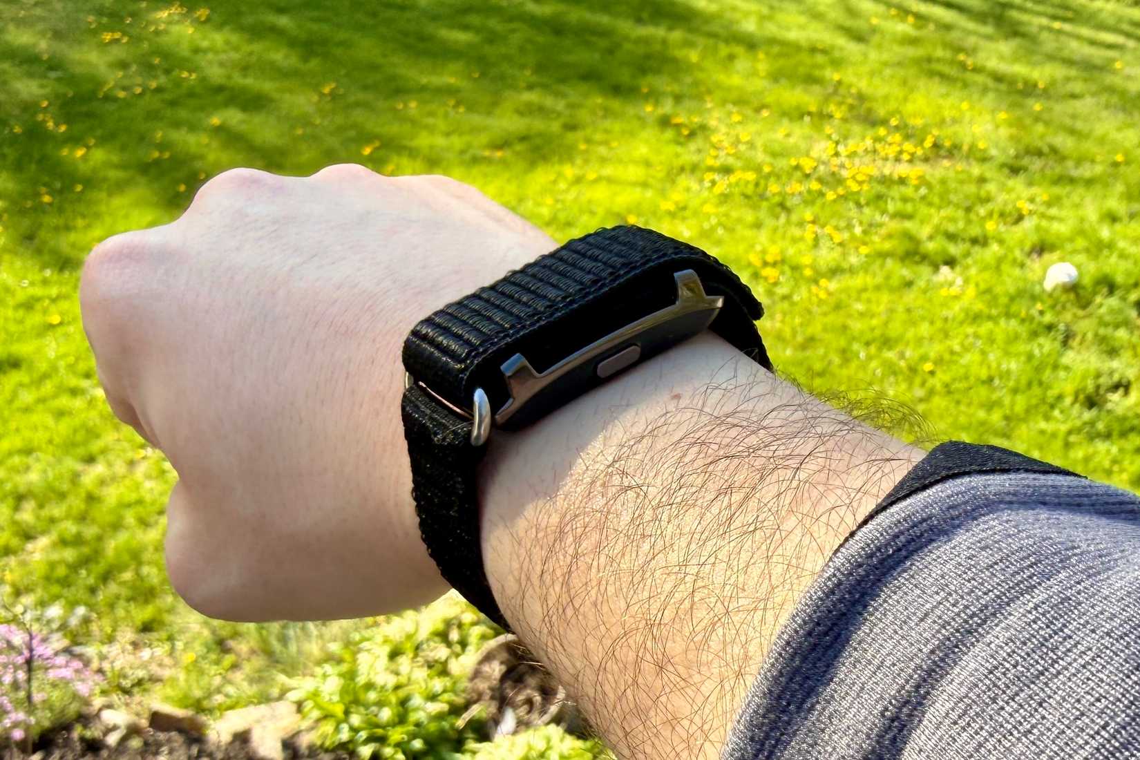 Qiunhang Smart Bracelet Fitness Tracker being worn in front of grass.
