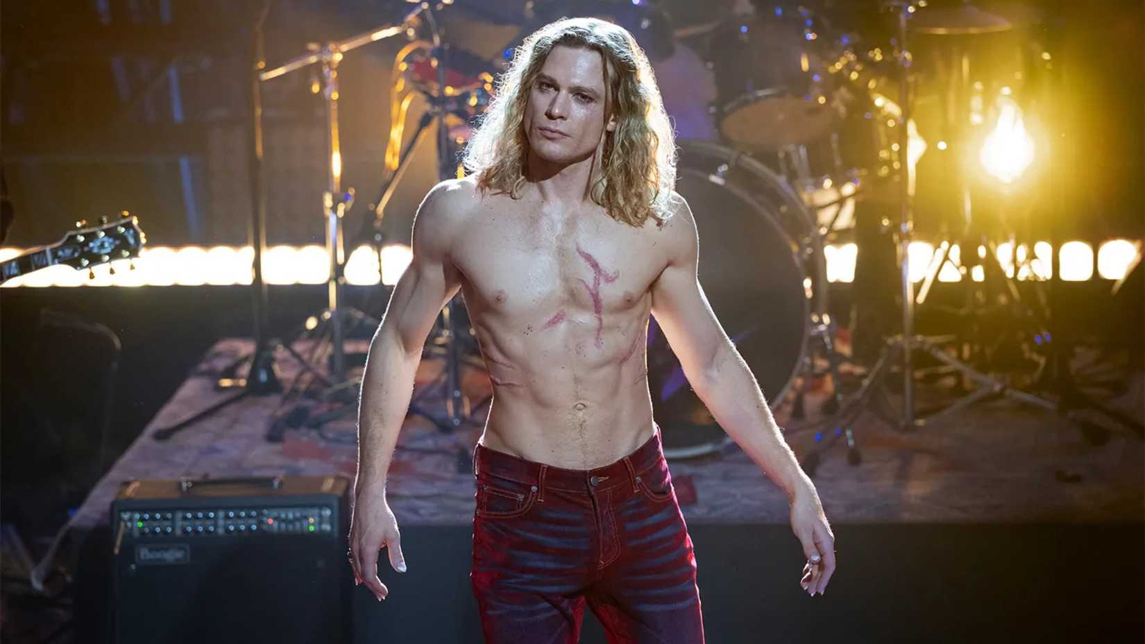 Sam Reid as a shirtless Lestat wearing red jeans, standing on stage in front of a drum set in The Vampire Lestat.