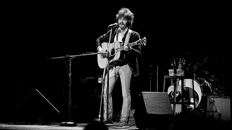 John Prine standing solo on stage with acoustic guitar at microphone
