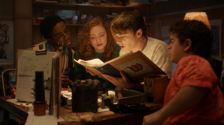 Caleb McLaughlin, Sadie Sink, Noah Schnapp, and Gaten Matarazzo as Lucas, Max, Will, and Dustin sitting at a table playing D&D in Stranger Things