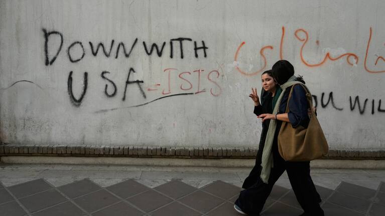 A woman reacts to the camera as she walks past an anti-U.S. graffiti painted on the wall of the British Embassy in Tehran, Iran