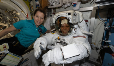 ESA astronaut Sophie Adenot and NASA astronaut Chris Williams smile at the camera. Adenot wears a teal polo shirt with a patch on the front. Williams is in a white spacesuit. They are on the International Space Station.