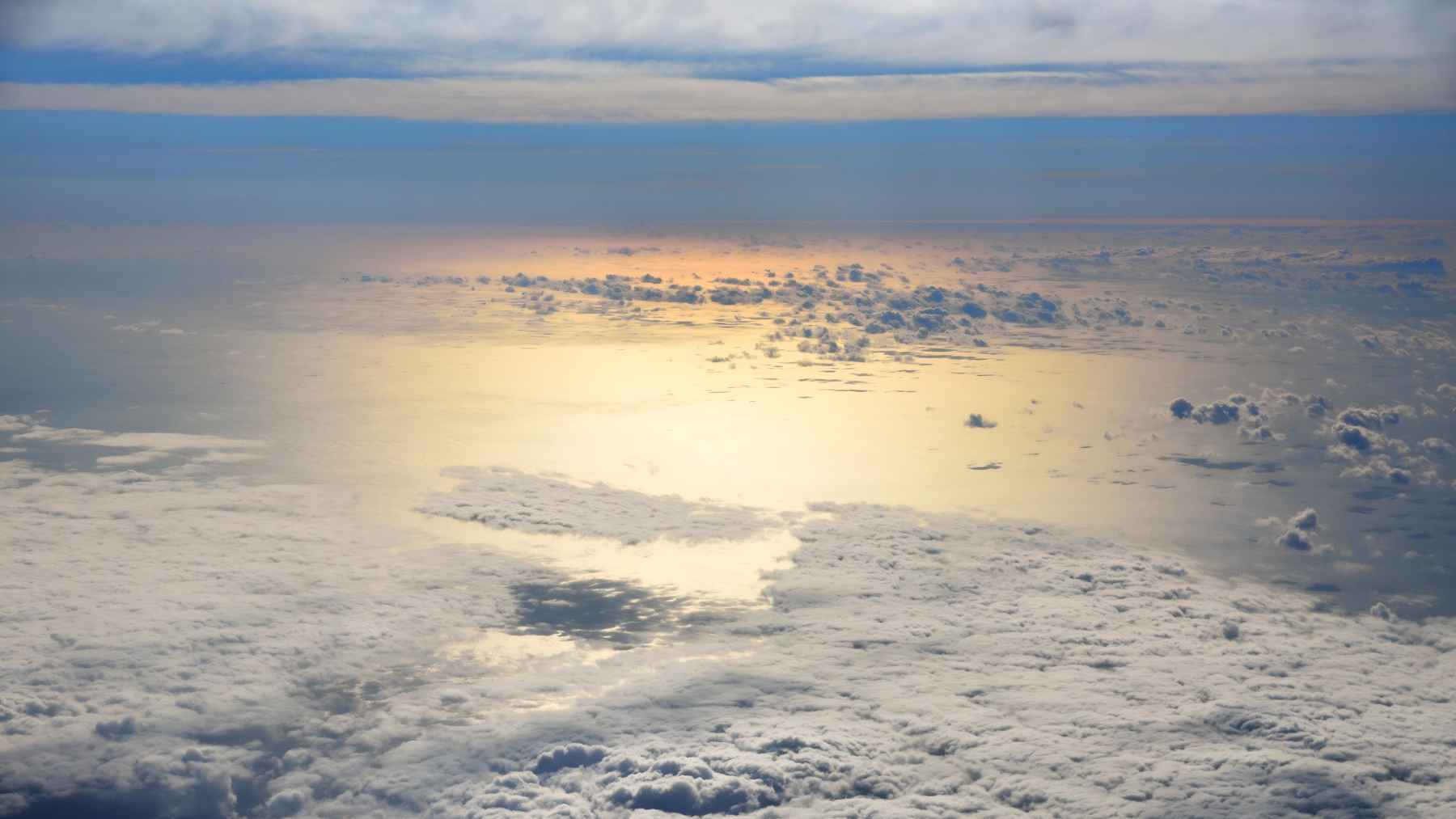 Aerial view of marine clouds over the ocean reflecting sunlight, with bright light reaching the water surface below.