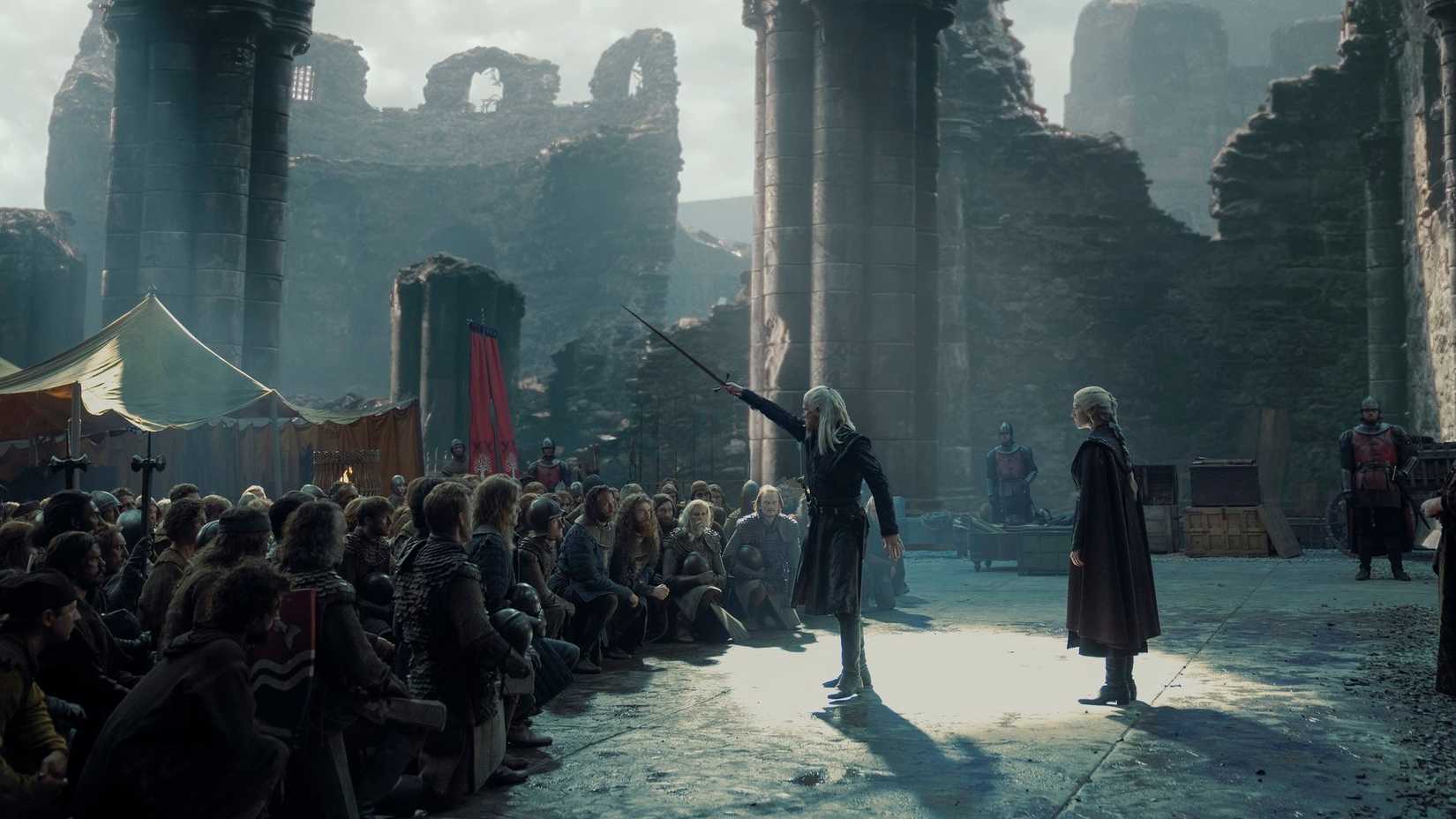 Daemon Targaryen (Matt Smith) holds up a sword in front of a kneeling crowd as Rhaenyra (Emma D'Arcy) stands behind him in in House of the Dragon season 2.