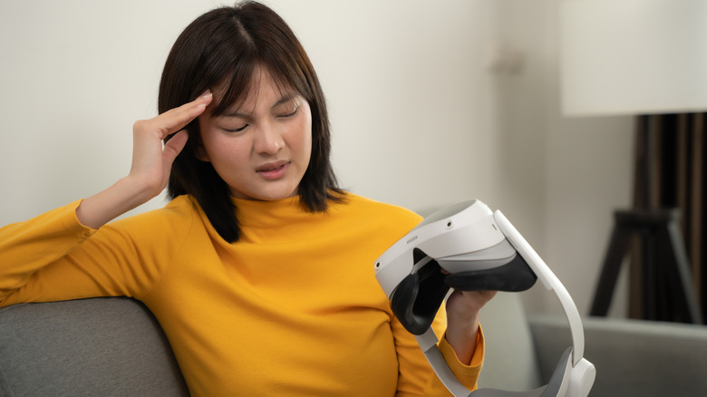 A woman grimaces while looking at her VR headset.