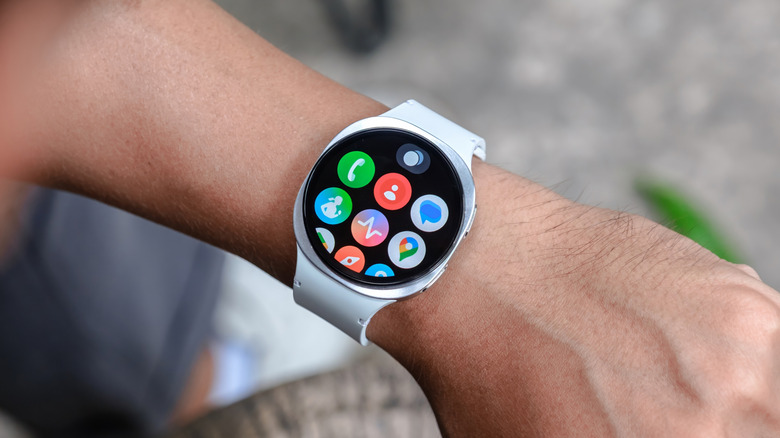 A silver Galaxy Watch Ultra with white band is being worn on a user's left wrist, the individual appears to be outside