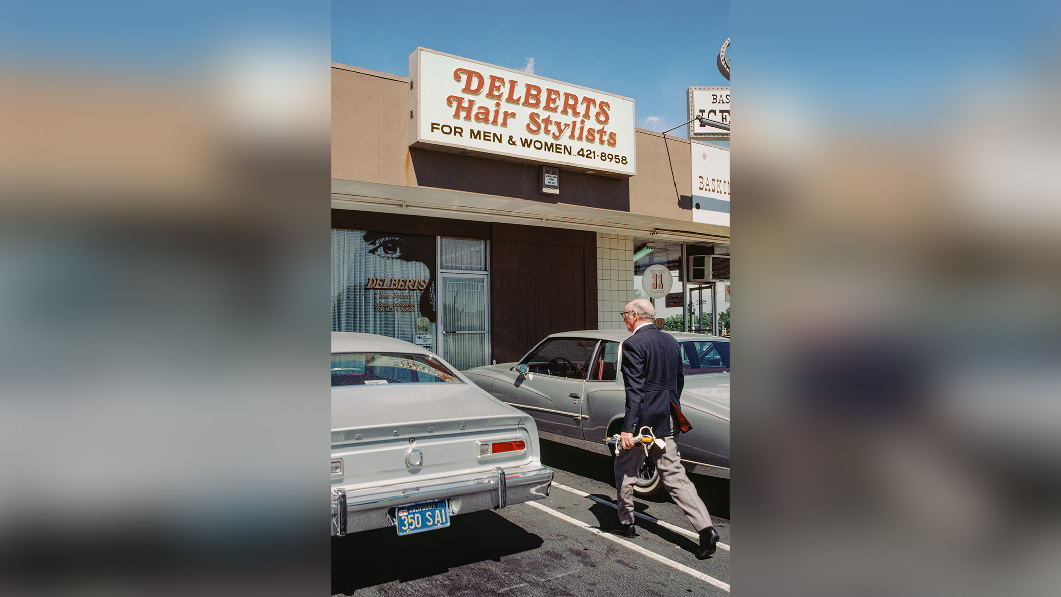 Man walks toward shop between parked cars.