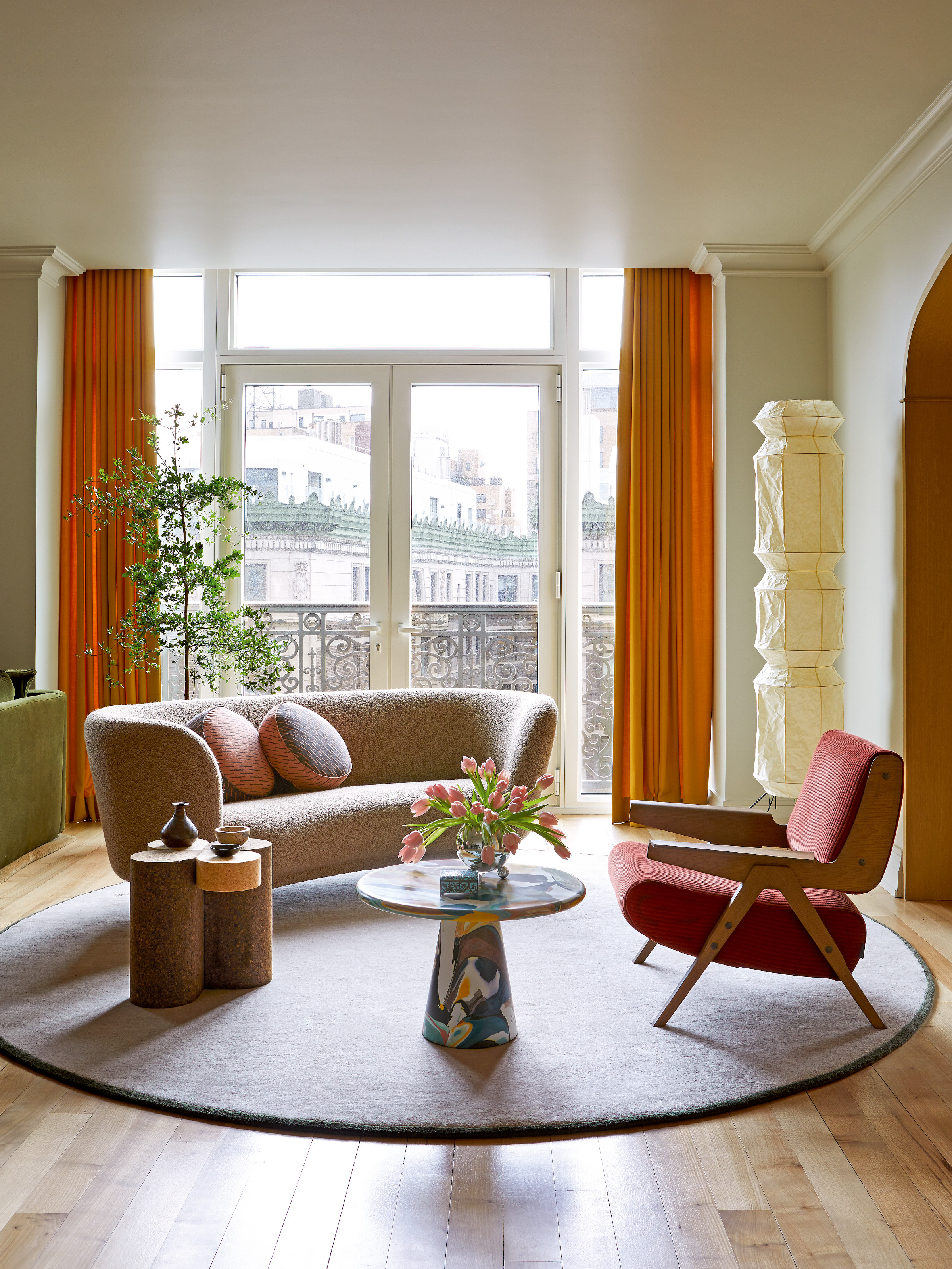 Sitting room with curved cream sofa, red and wood armchair, paper floor lantern, multicolour coffee table and round rug
