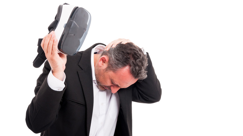 A man rubs the back of his next while holding a VR headset.