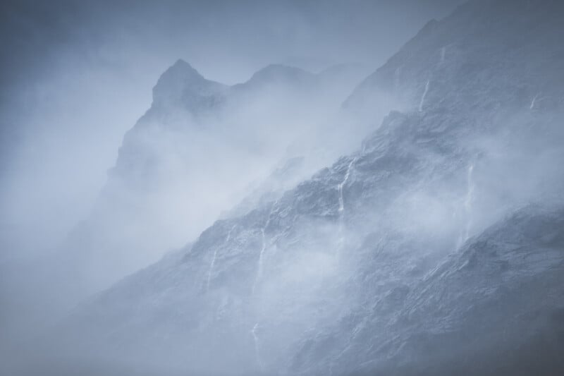 Misty mountain peaks rise dramatically, partially obscured by thick fog. The dark, rugged rock faces are faintly visible through the mist, creating a moody and mysterious atmosphere.