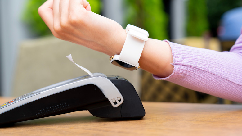 A person holding their smartwatch's face against a scanner to pay using NFC