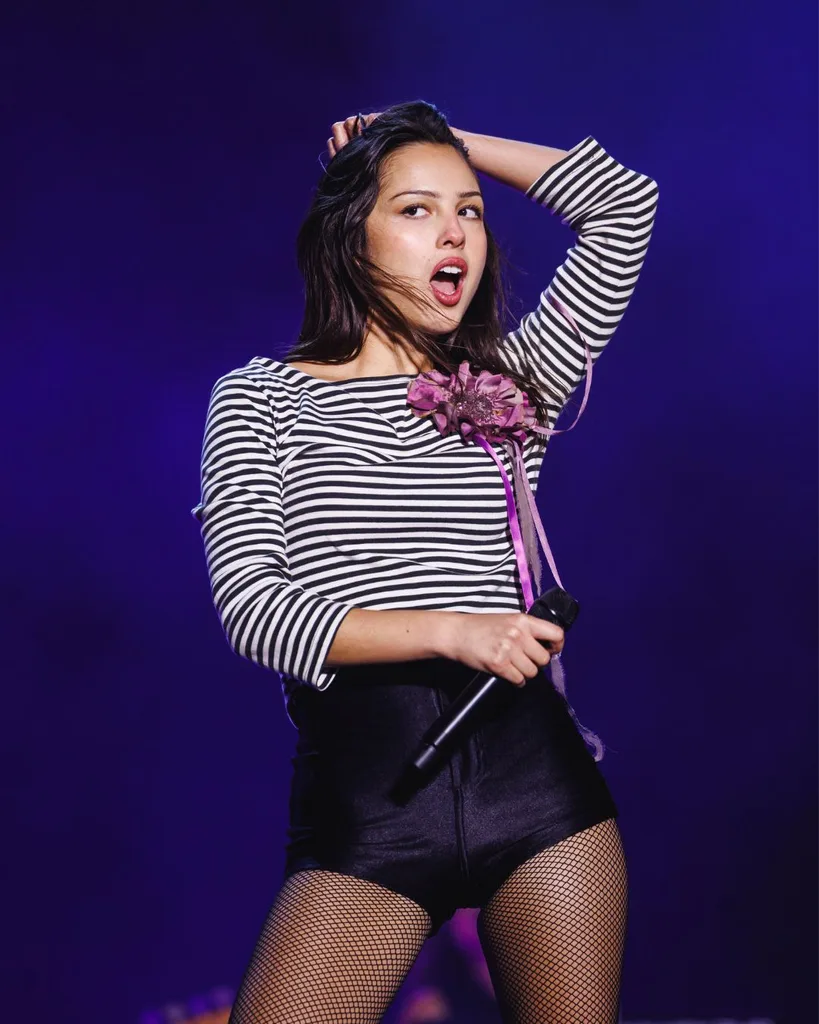 Olivia Rodrigo performing on stage in a black and white striped top and black hotpants