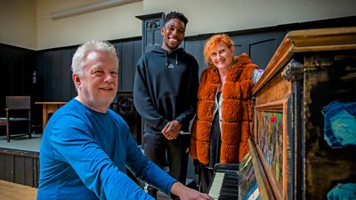Three people smiling around a piano