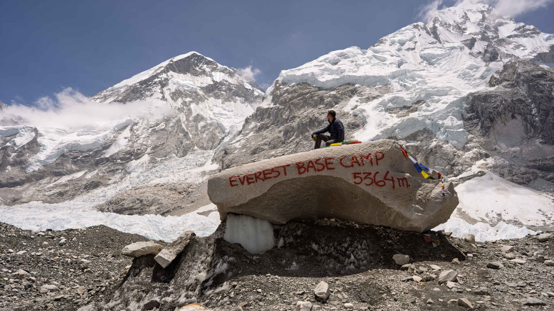 a person sits on top of a large boulder that reads "Everest Base Camp 5364 m"