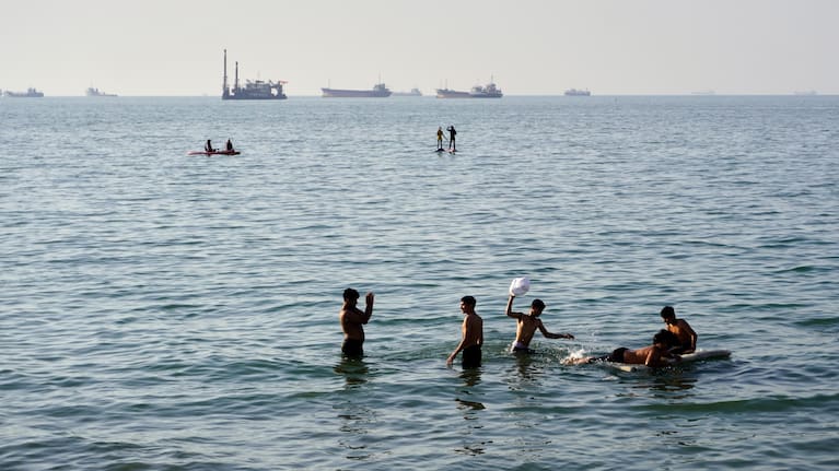Residents swim and play in the waters of the Strait of Hormuz while cargo ships and commercial vessels lie anchored in the distance off Bandar Abbas, Iran, Wednesday, June 10, 2026.