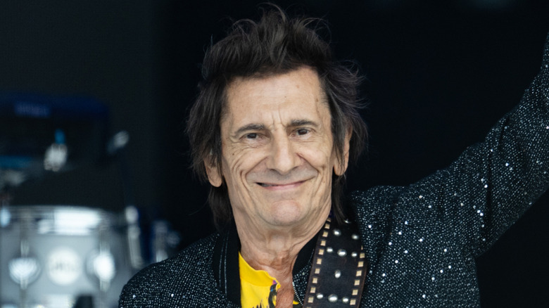 Ronnie Wood grinning onstage and holding up arm