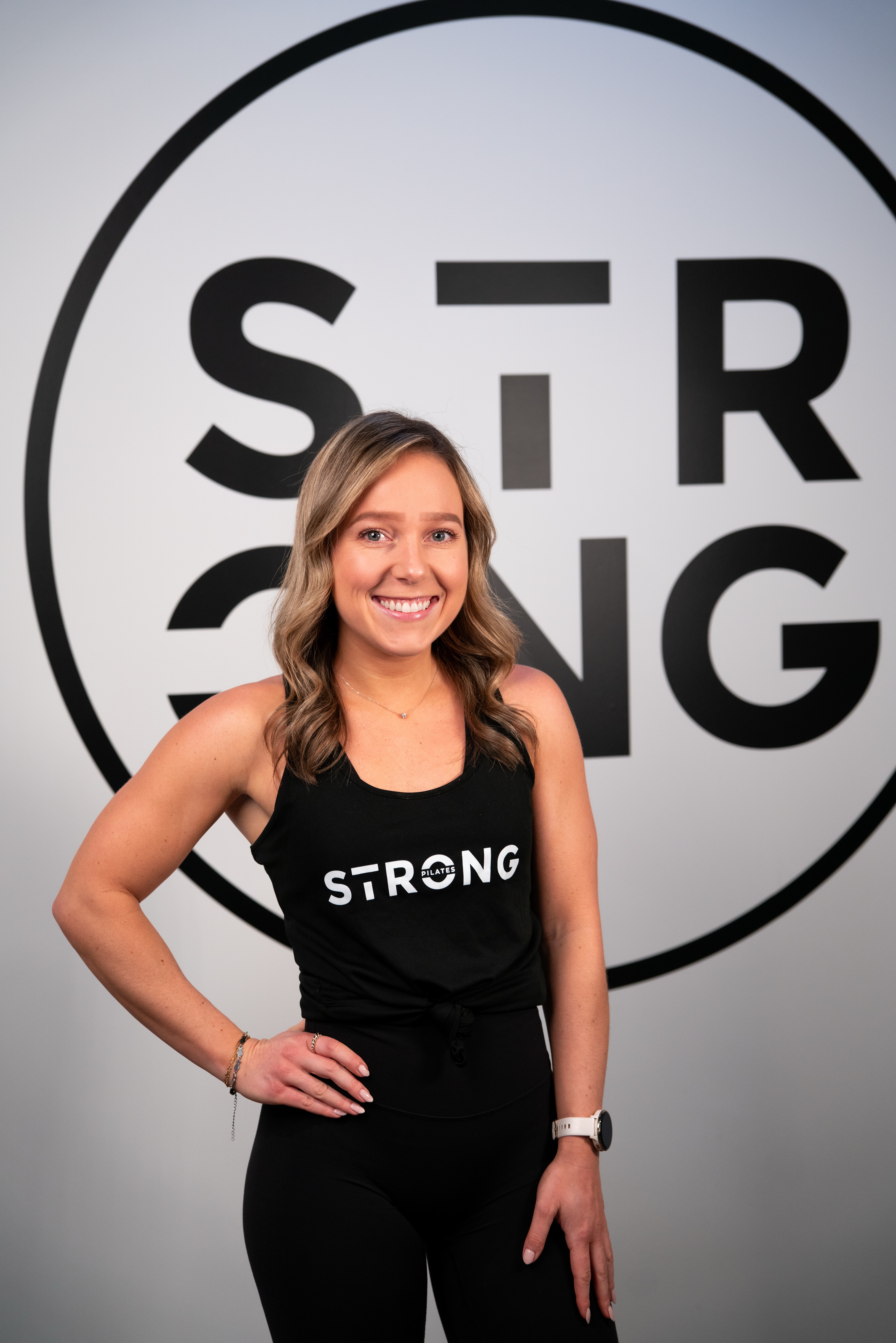 woman facing the camera smiling wearing a black vest with strong written on it