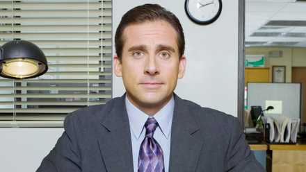 Steve Carell as Michael Scott sitting at a desk in 'The Office'