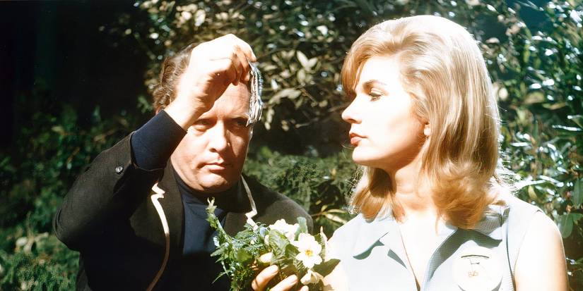 Number Six sitting near a blonde woman who's holding flowers in The Prisoner