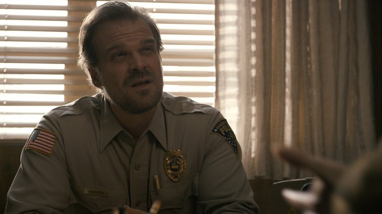 David Harbour as Hopper sitting at a desk in Stranger Things