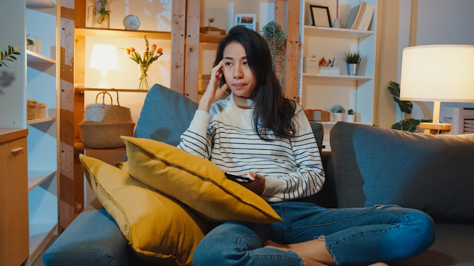 Woman sitting alone at home looking at her phone, showing how anxiety and avoidance can shrink your world