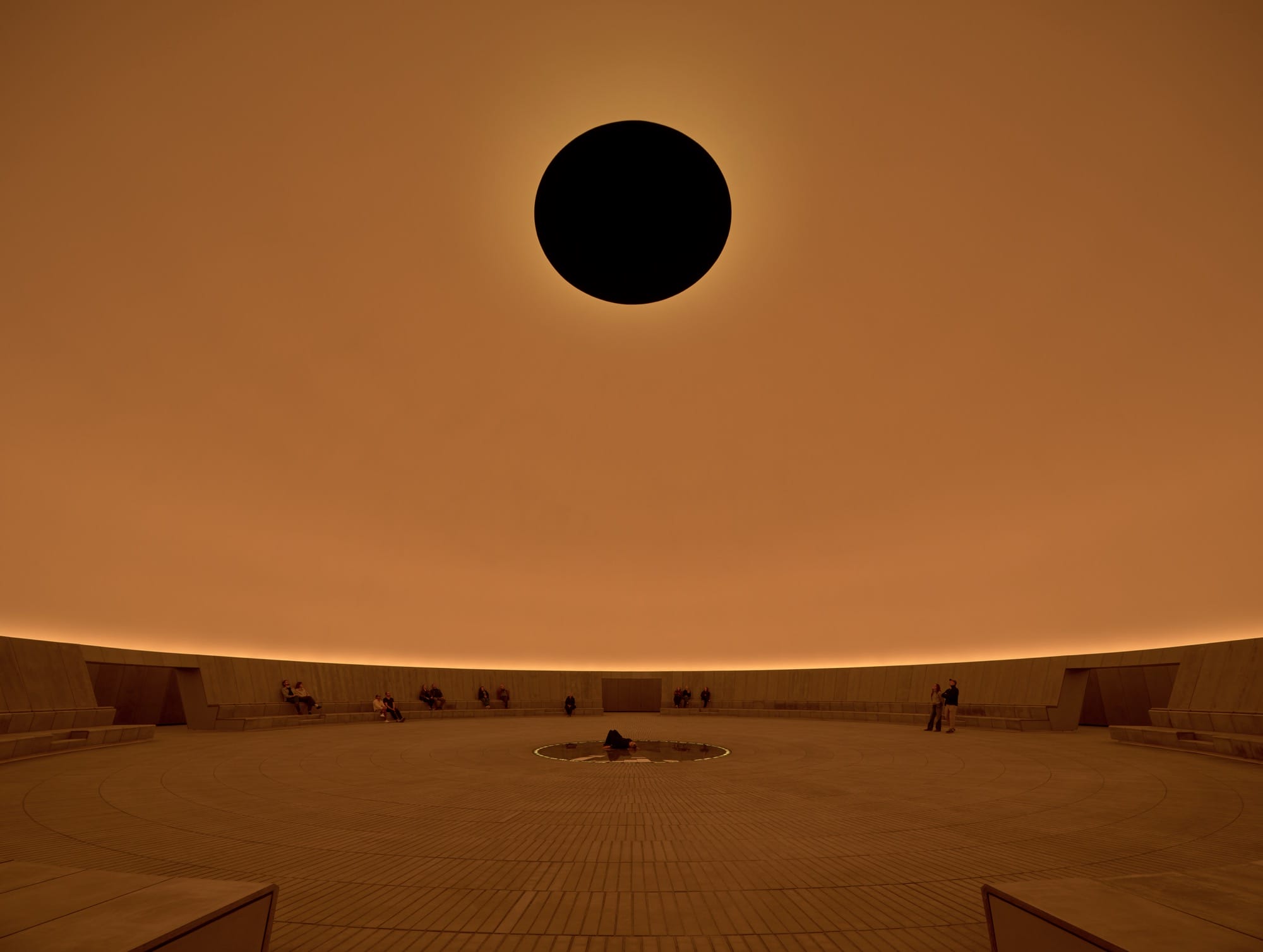 a large-scale light exhibition by James Turrell featuring a black hole in an orange dome