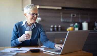A retiree seated at a table is using a laptop.