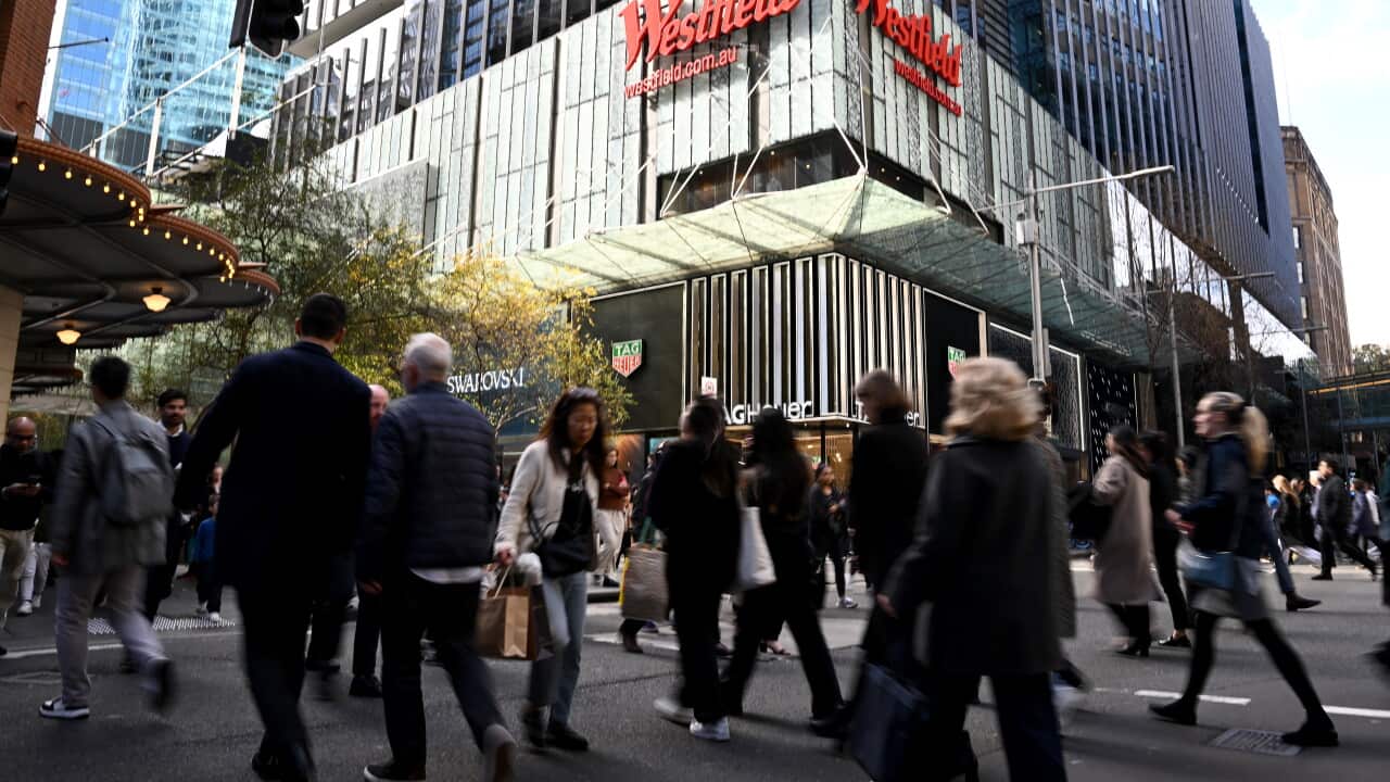 People walk across a city street with highrise buildings seen in the background