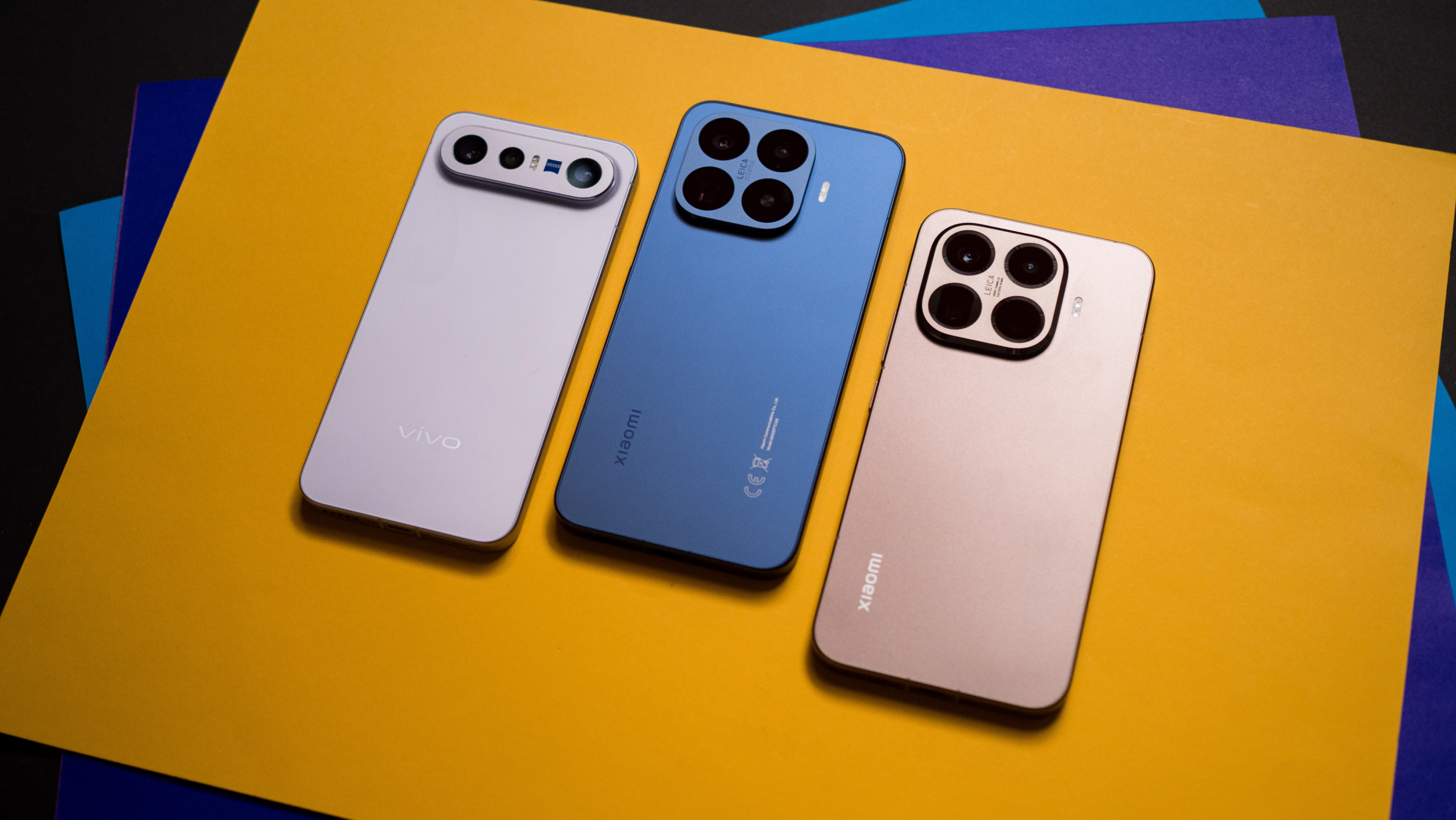 Xiaomi 17T Pro, Vivo X300 FE, and 15T Pro rear view against a colorful craft sheet highlighting the design