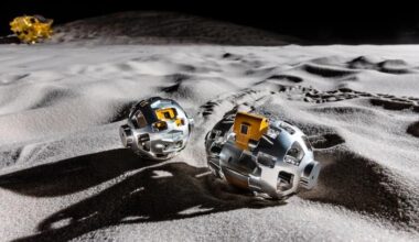 A close up of an oval shaped metal roller with a camera in the middle rolling on a sandy surface.