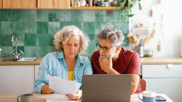 Senior husband and wife paying bills and managing family finances together on a laptop, discussing expenses in a cozy home environment.