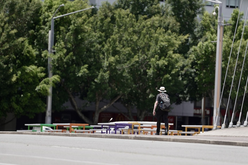 Person walks alone wearing dark clothes, white hat and a backpack.