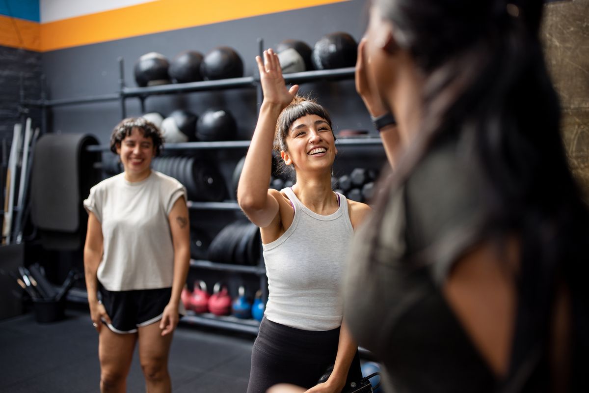 Group of young people interchange high-five after workout in the cross training gym. Multiracial group of gym friends celebrating successful workout at cross training gym.