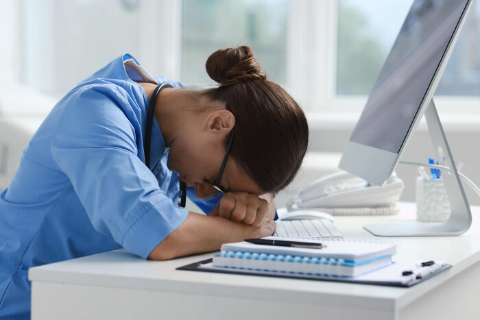 A medical professional, exhausted, rests her head on her desk, illustrating the challenging medical industry.