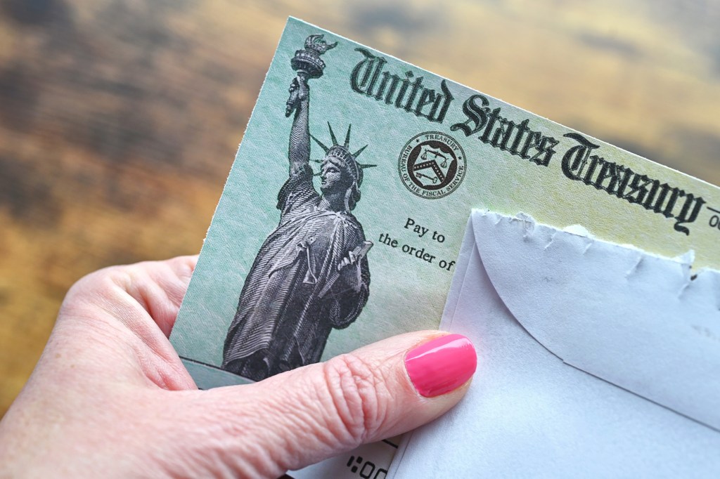 A person's hand with pink nail polish holding a United States Treasury check with an image of the Statue of Liberty.