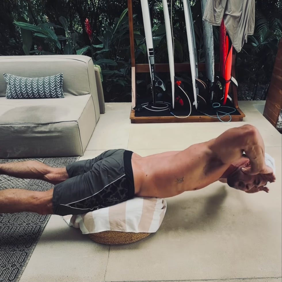 person doing back exercise on a cushion near surfboards and a couch. person doing back exercise on a cushion near surfboards and a couch.