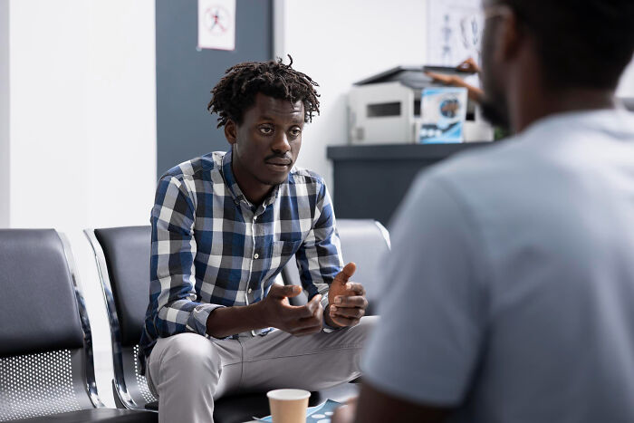 Two men in a waiting room having a serious conversation, revealing uncomfortable truths about the medical industry.
