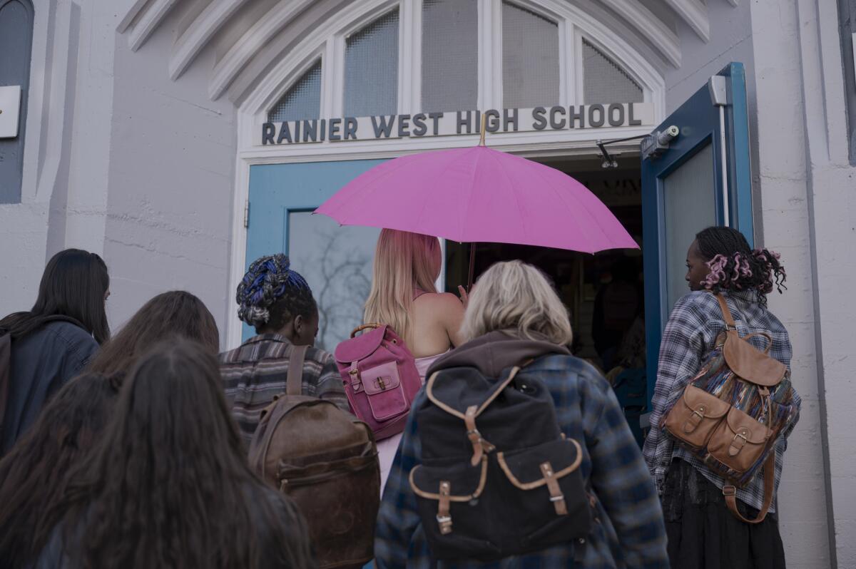 A group of students walking into the entrance of a high school with one person holding a bright pink umbrella.