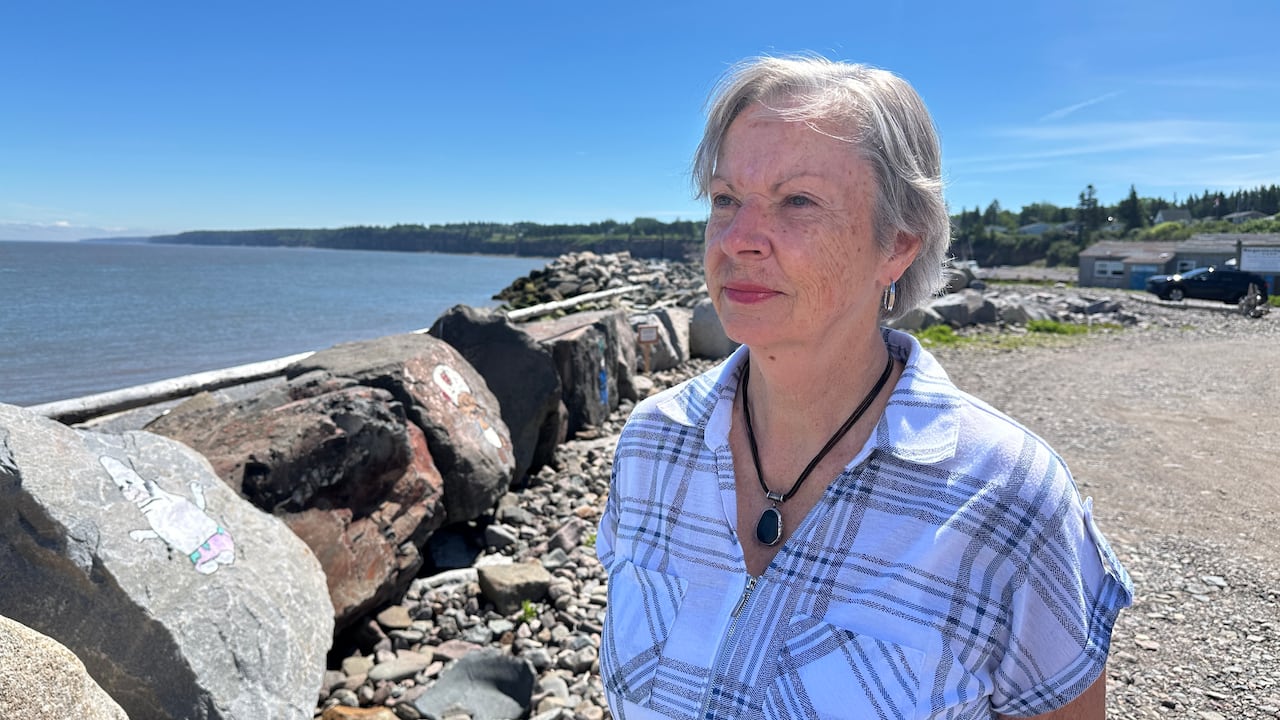 A woman stands between a gravel road and large boulders next to the Bay of Fundy.