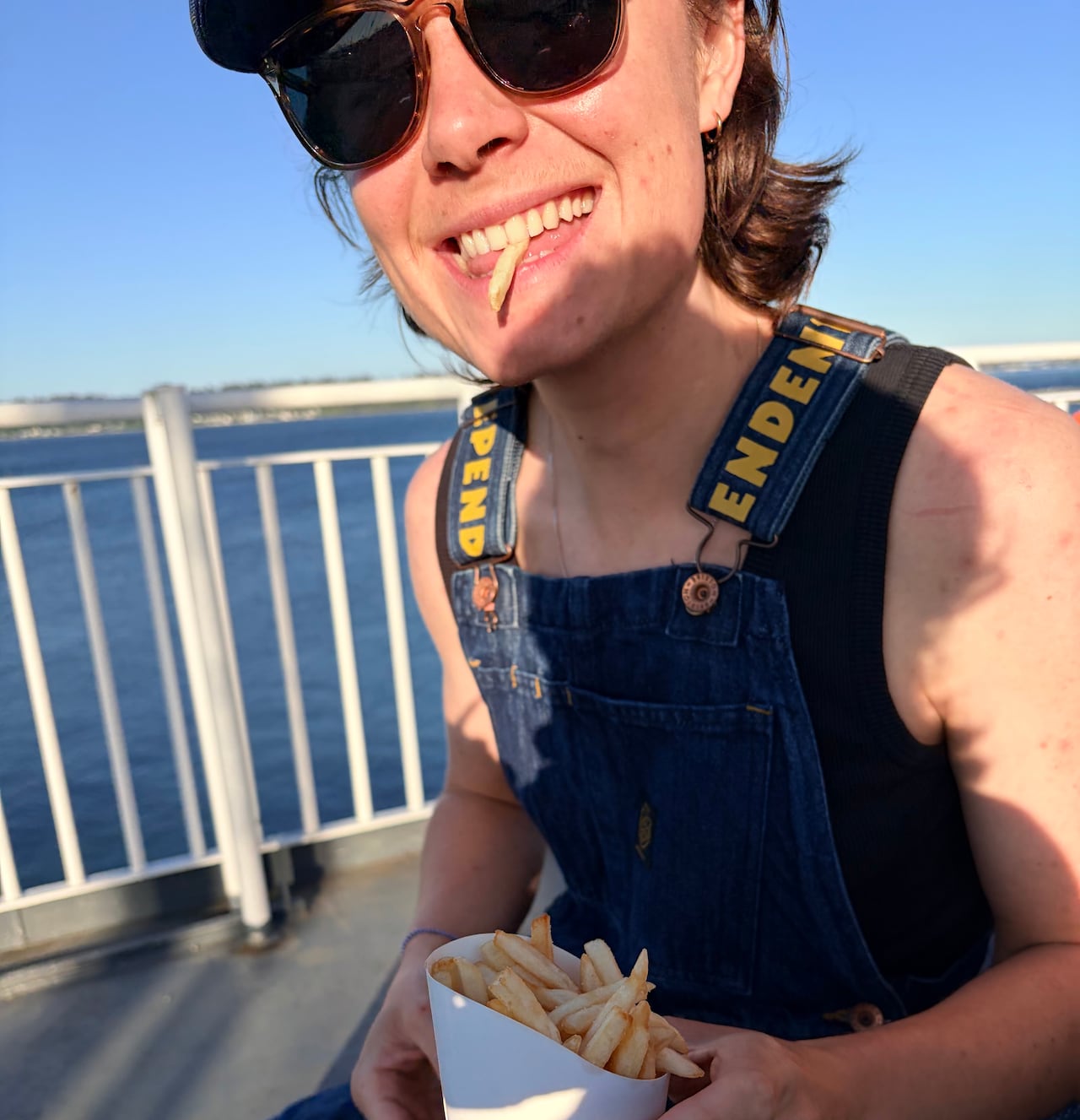 A person sits eating fries near the water