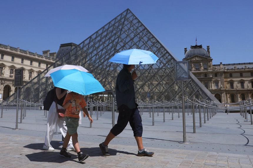 Tourists protecting themselves from the sun under umbrellas walk past the glass Pyramid of the Louvre museum in Paris on June 24.