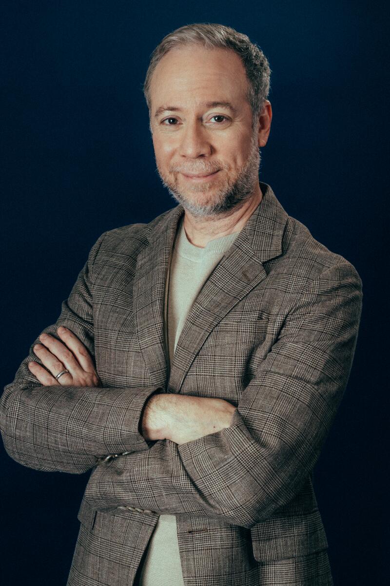A smiling man with a beard standing with his arms folded across his chest.