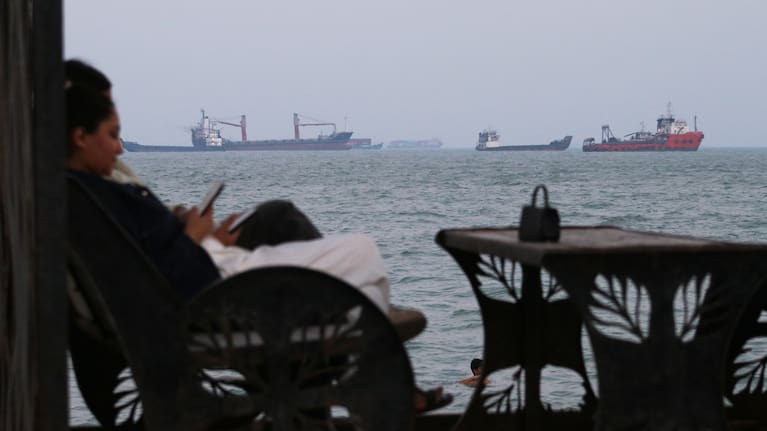 Residents check their cellphones as they sit at a cafe overlooking commercial vessels anchored in the Strait of Hormuz, off Bandar Abbas, Iran, Sunday, July 12, 2026.