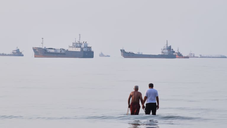 Two men wade in the waters of the Strait of Hormuz with vessels anchored in the background, off Bandar Abbas, Iran, Sunday, July 12, 2026.