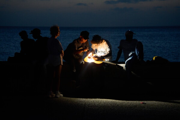 A man repairs a guitar string by the light of a flashlight on the Malecon seawall during a blackout in Havana, Cuba, Tuesday, July 14, 2026. (AP Photo/Ramon Espinosa)